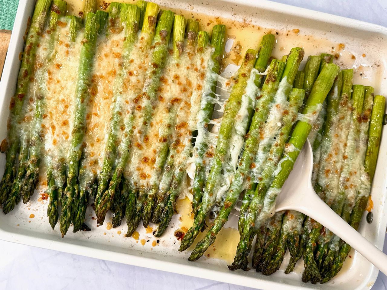 Cheesy Roasted Asparagus on a baking sheet with a white spatula