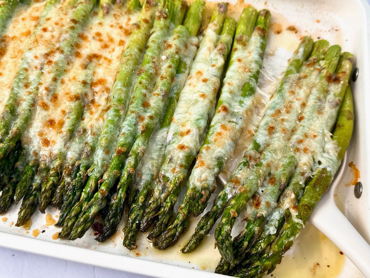 Cheesy Roasted Asparagus on a baking sheet with a white spatula