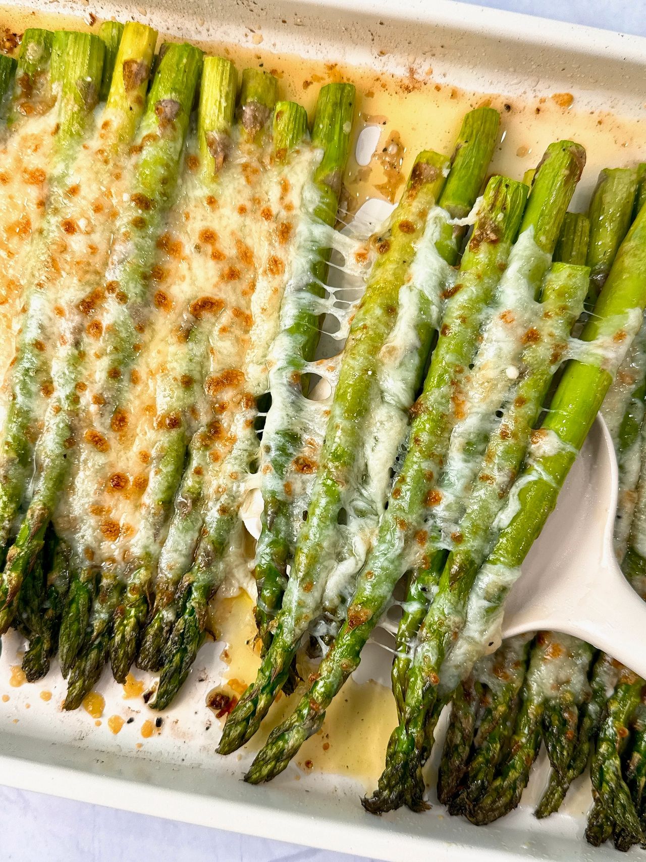 Cheesy Roasted Asparagus on a baking sheet with a white spatula