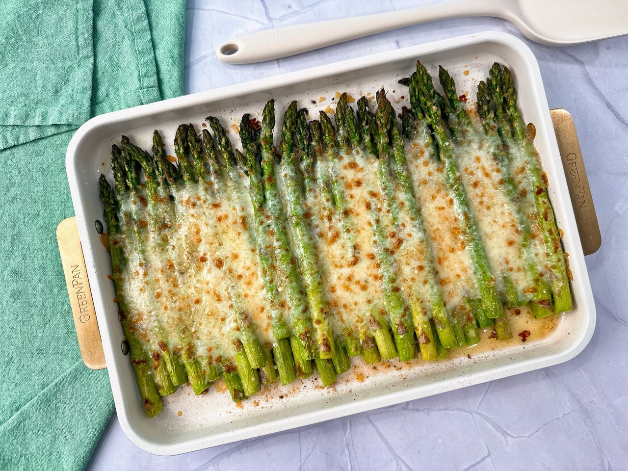 Cheesy Roasted Asparagus on a baking sheet with a white spatula