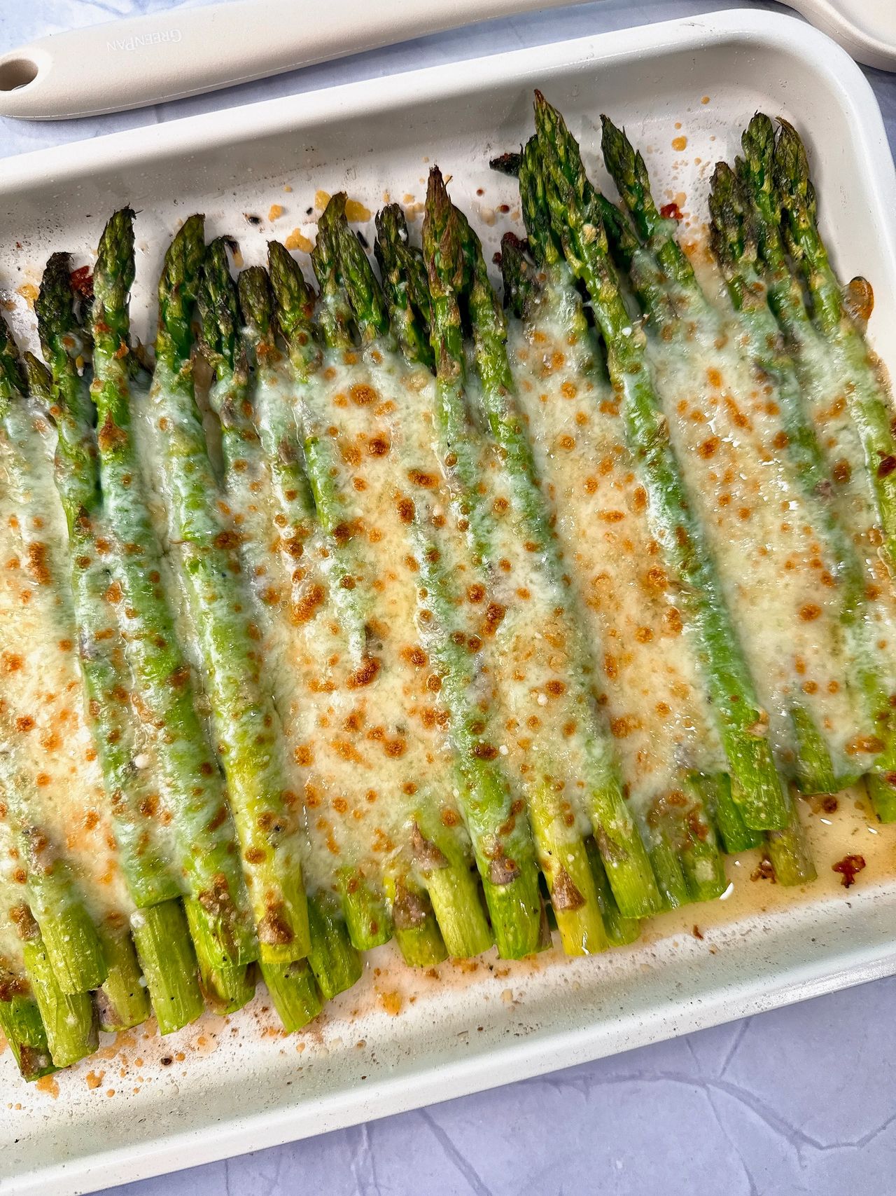 Cheesy Roasted Asparagus on a baking sheet with a white spatula