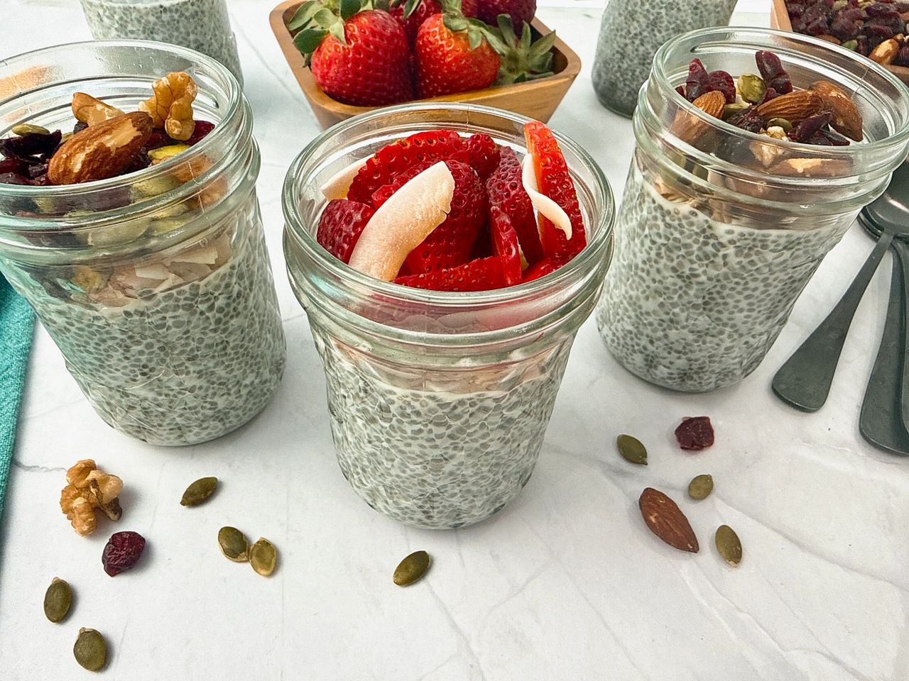 Chia Seed Pudding in mason jars with black spoons, fresh fruit, and granola