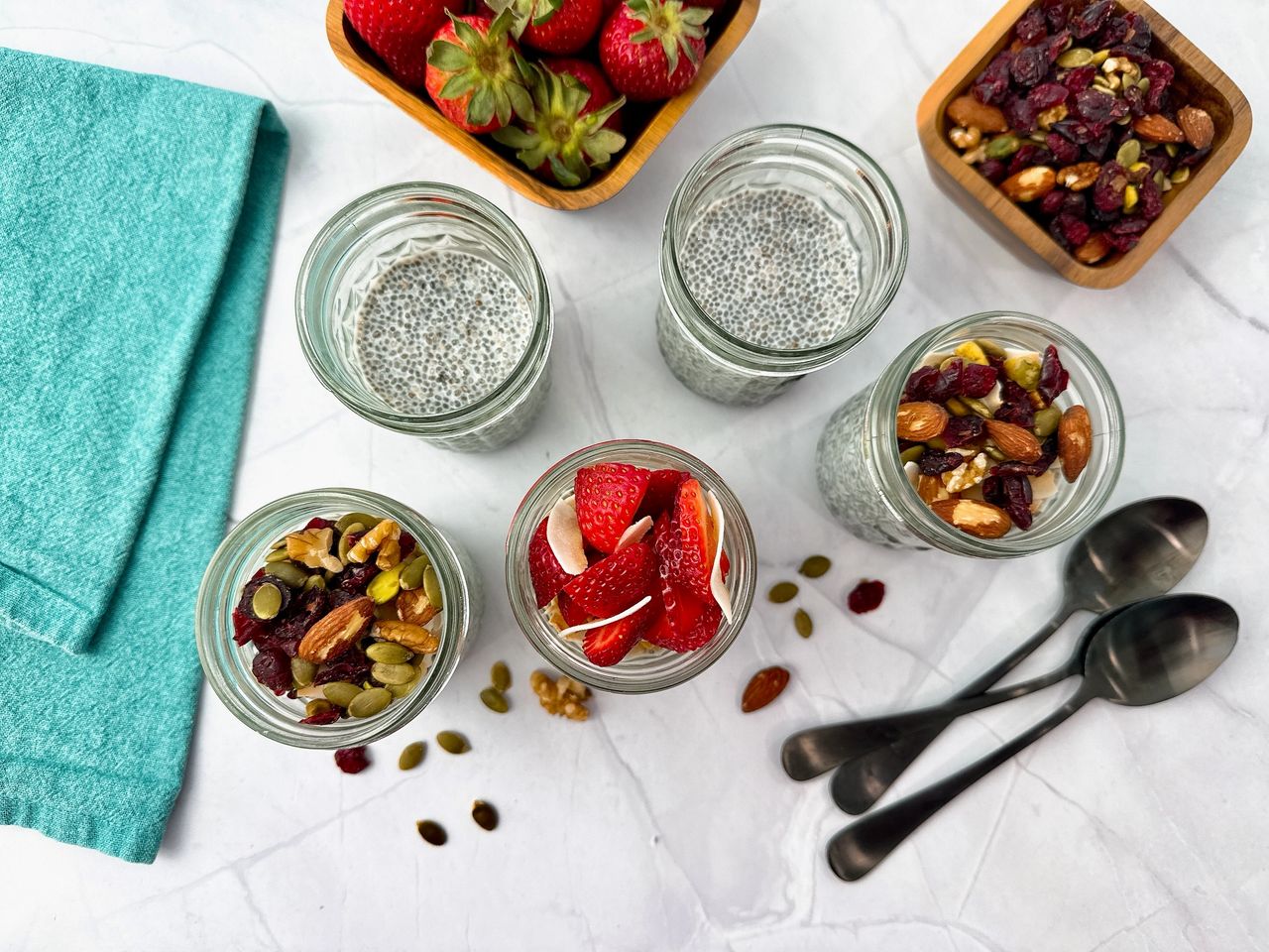 Chia Seed Pudding in mason jars with black spoons, fresh fruit, and granola