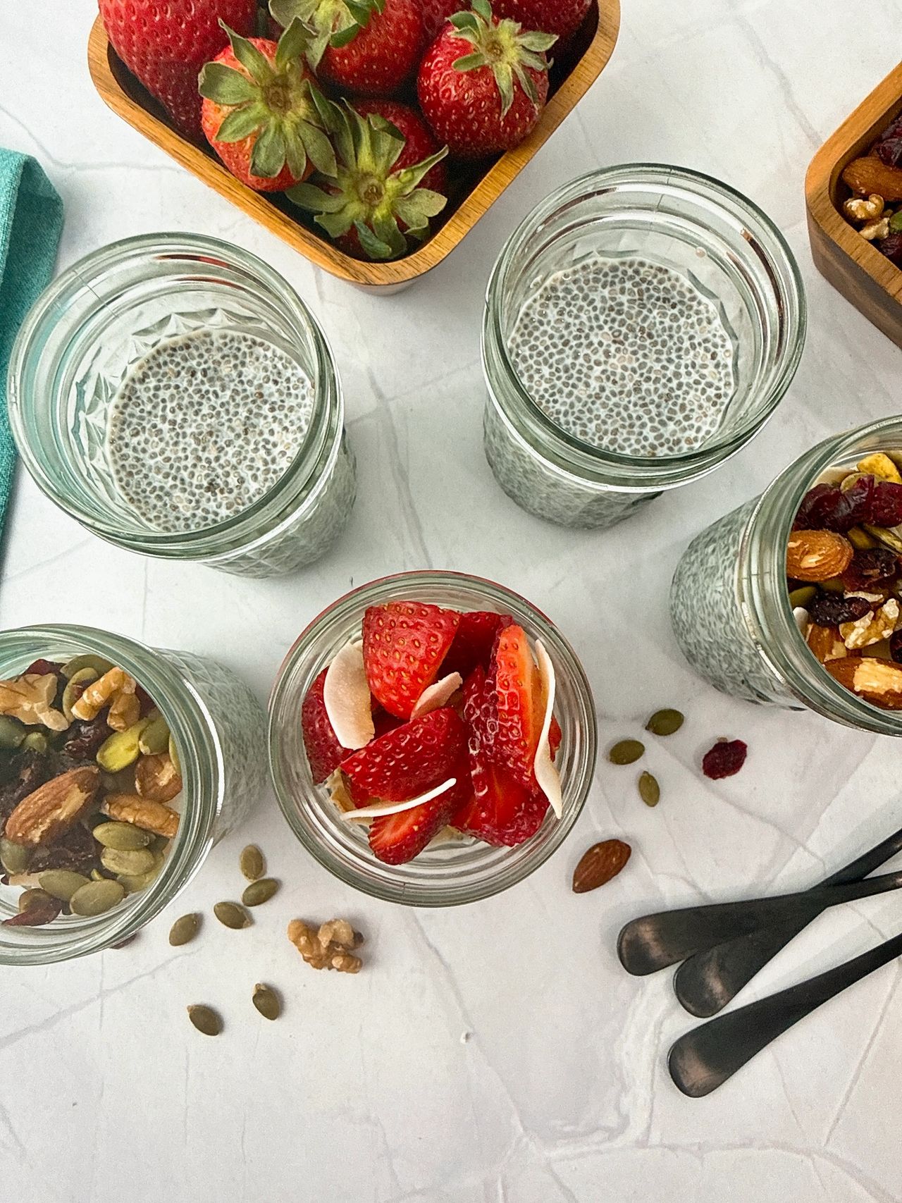 Chia Seed Pudding in mason jars with black spoons, fresh fruit, and granola