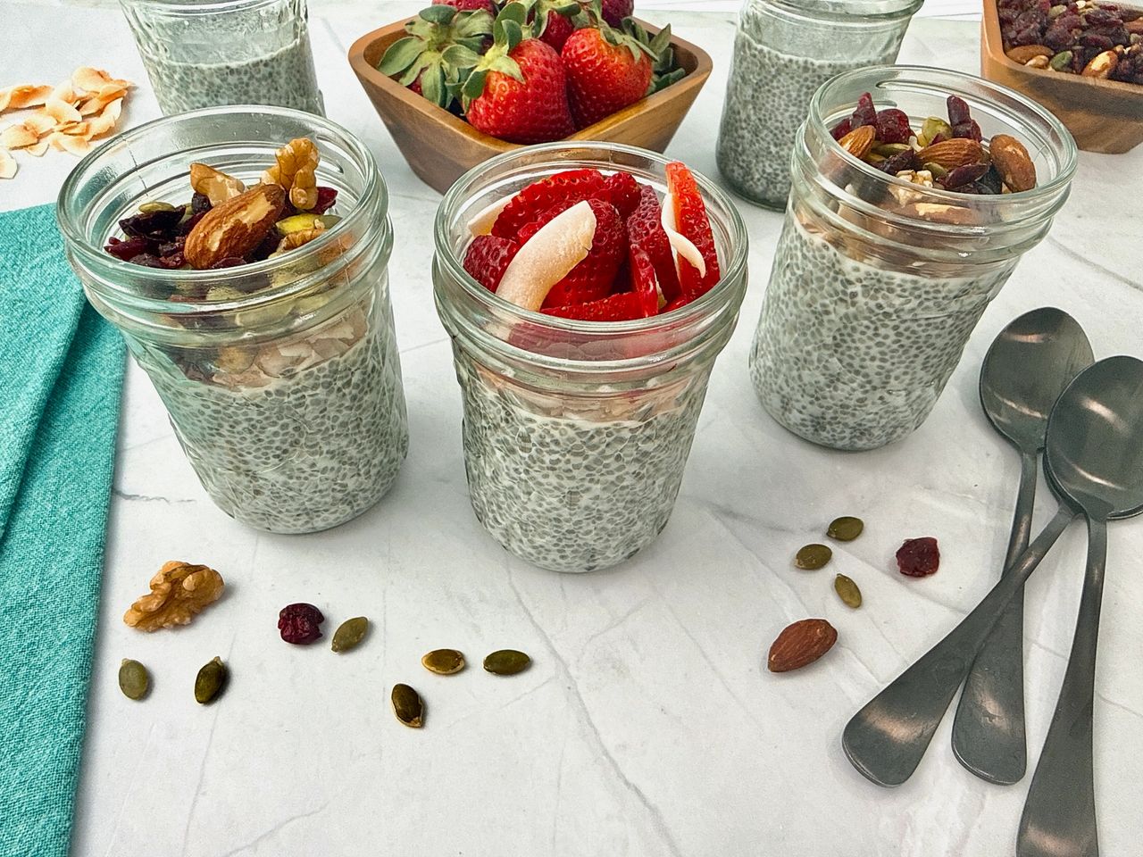 Chia Seed Pudding in mason jars with black spoons, fresh fruit, and granola