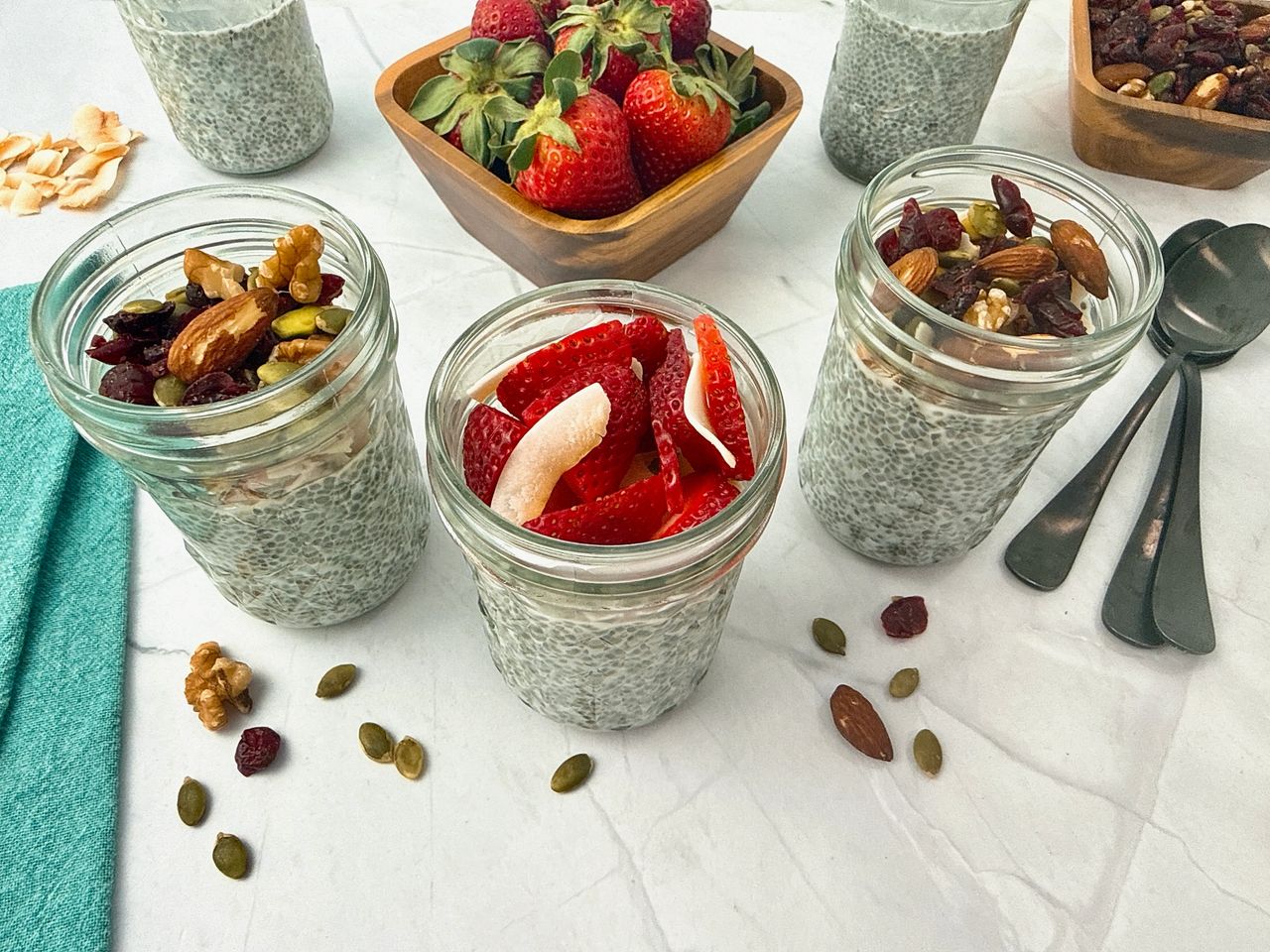 Chia Seed Pudding in mason jars with black spoons, fresh fruit, and granola