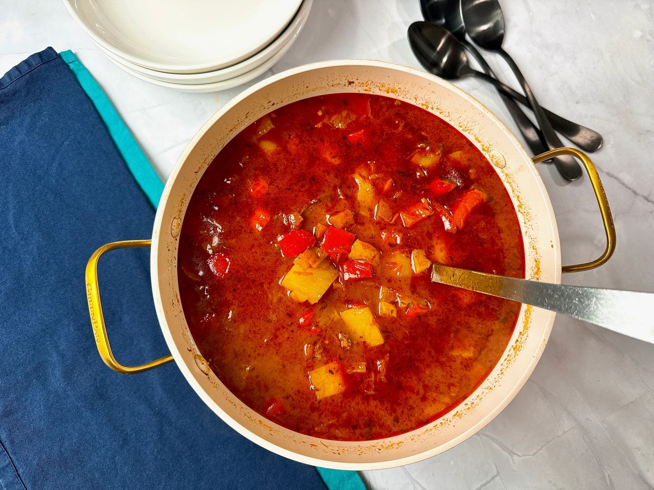 Hungarian Goulash in stock pot with white bowls, black spoons, and blue napkins