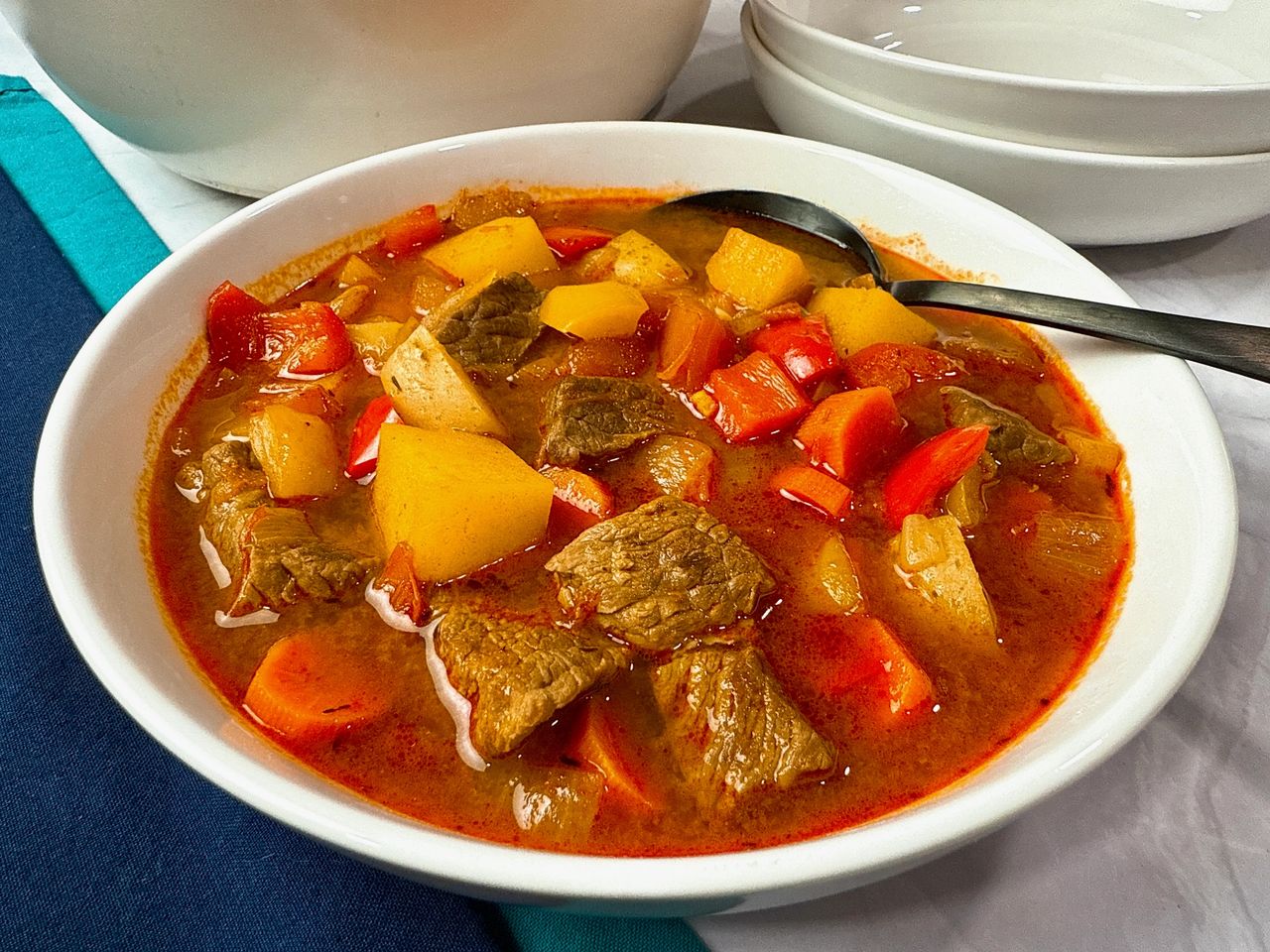 Hungarian Goulash in a white bowl with a black spoon and blue napkins