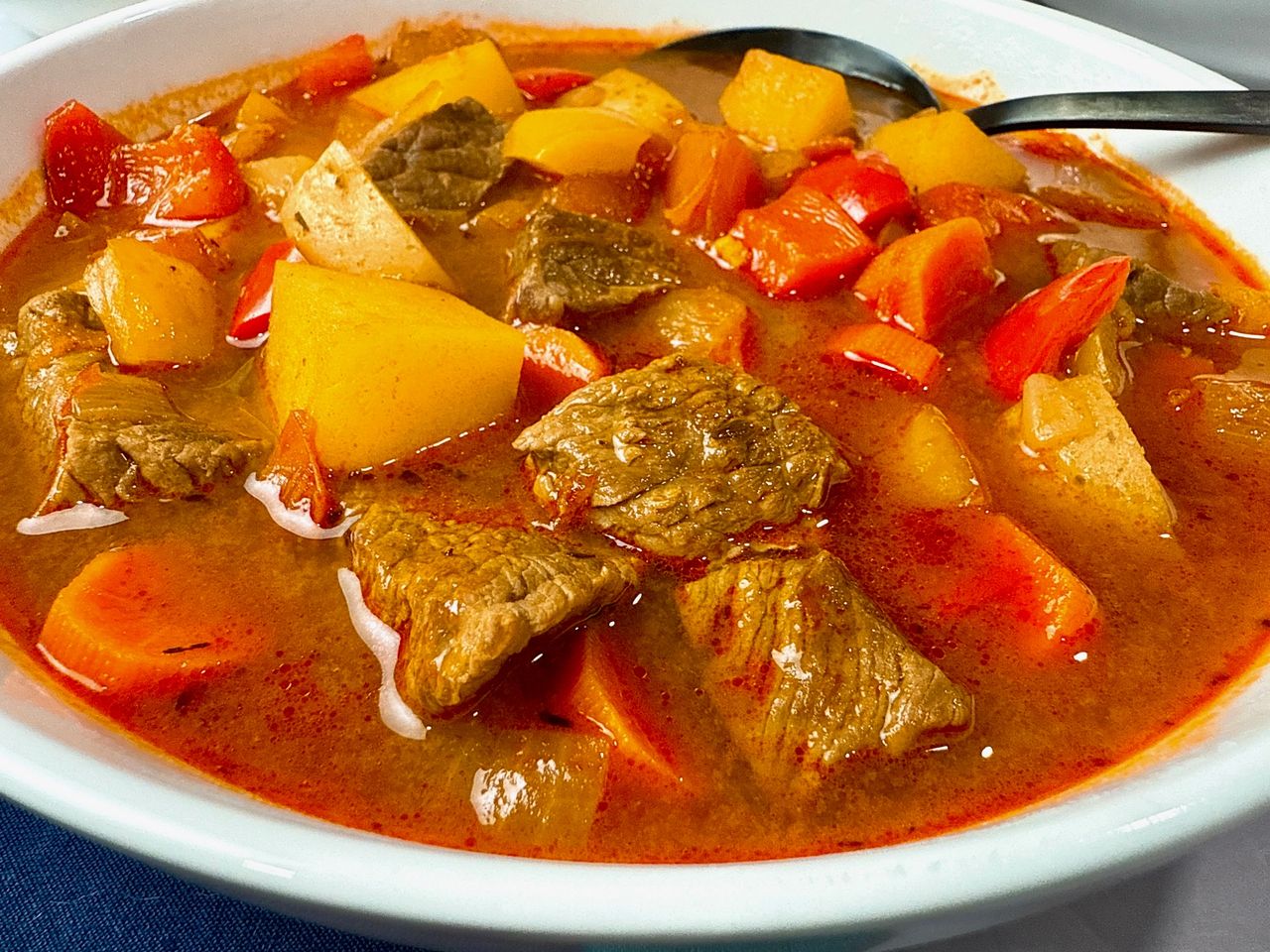 Hungarian Goulash in a white bowl with a black spoon and blue napkins