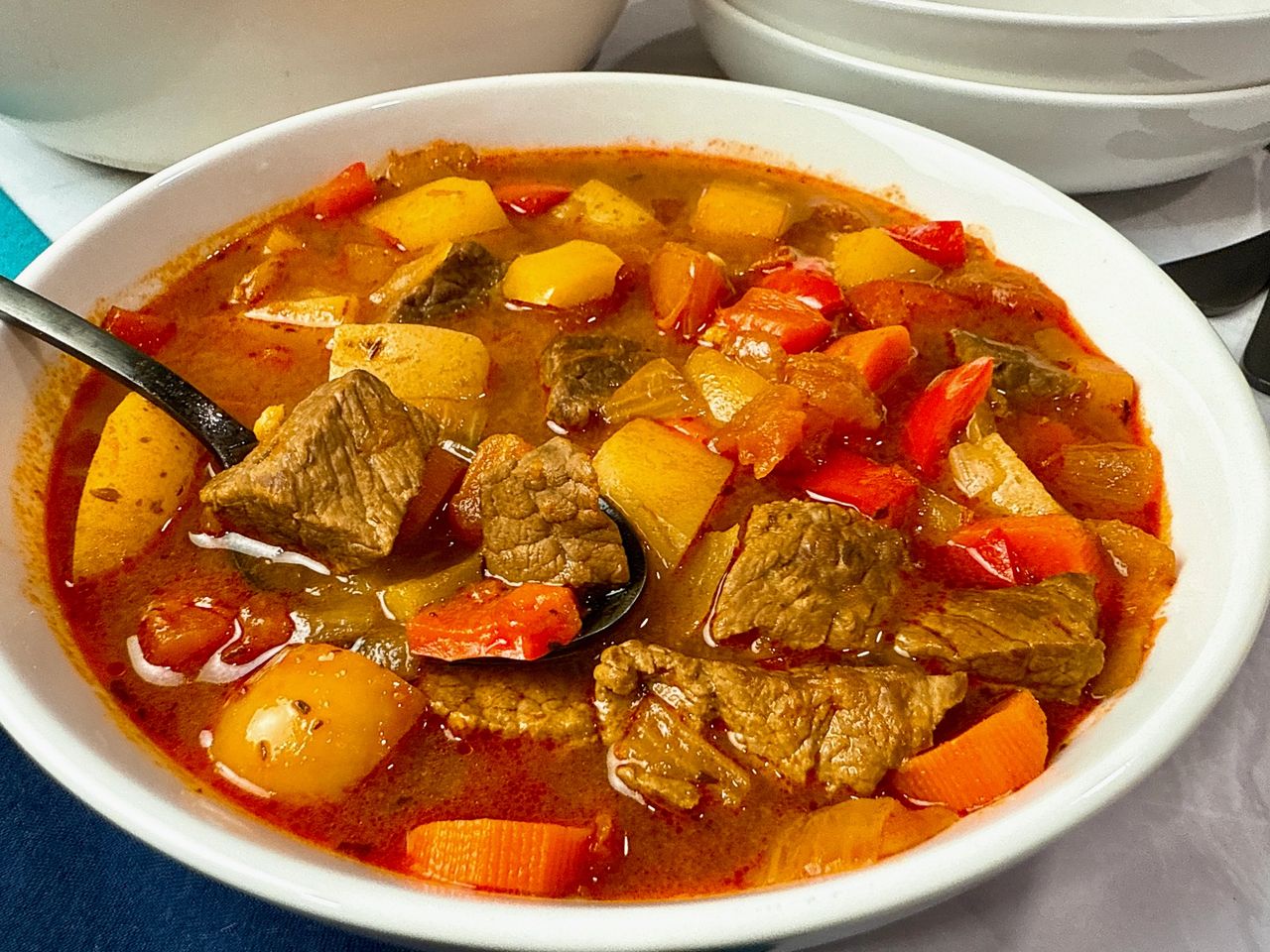 Hungarian Goulash in a white bowl with a black spoon and blue napkins