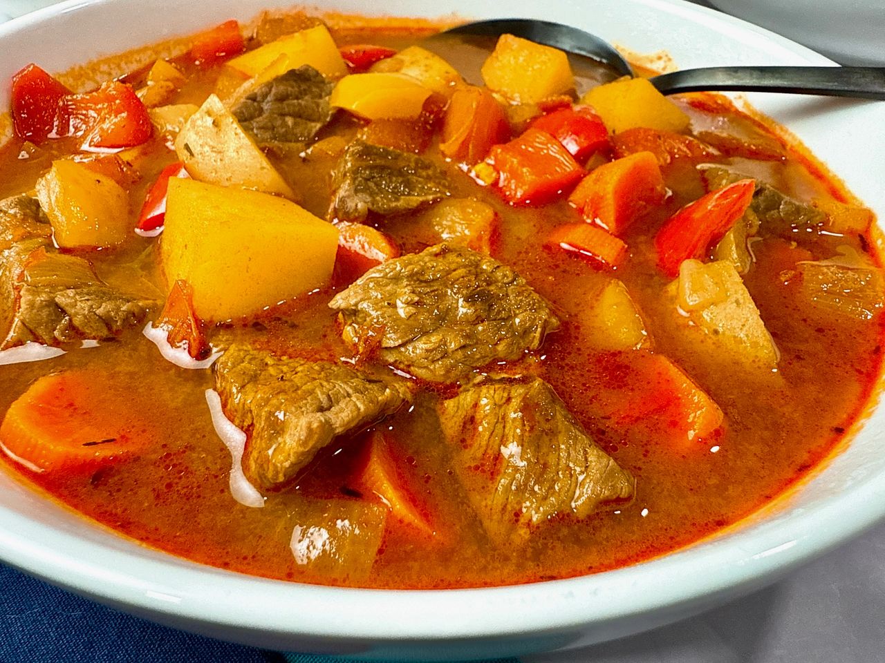 Hungarian Goulash in a white bowl with a black spoon and blue napkins