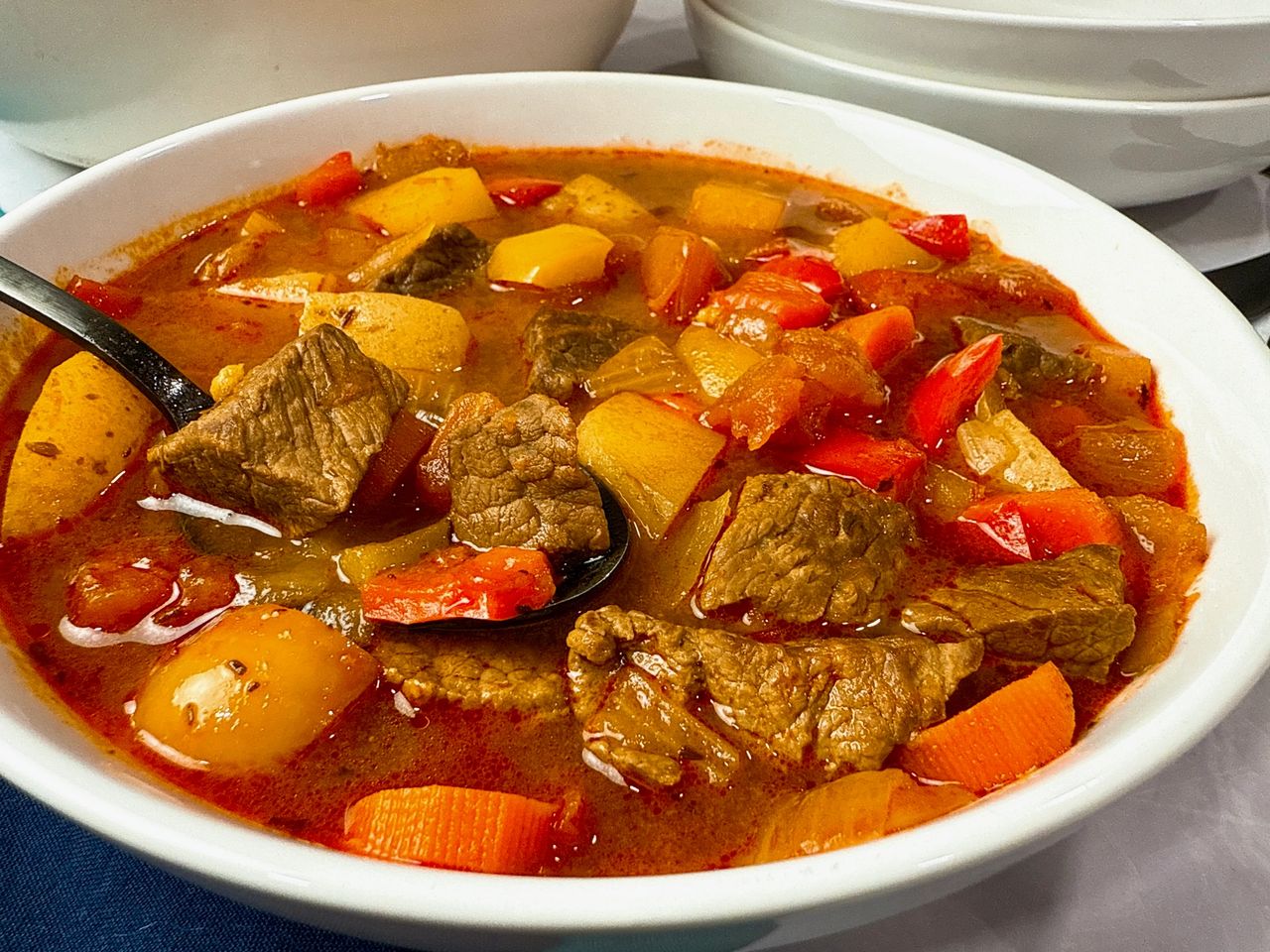 Hungarian Goulash in a white bowl with a black spoon and blue napkins