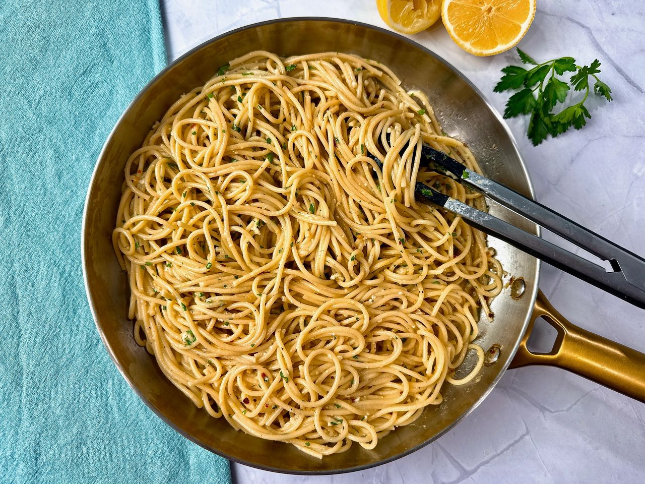 Lemon Garlic Pasta in skillet with tongs, parsley, and lemon