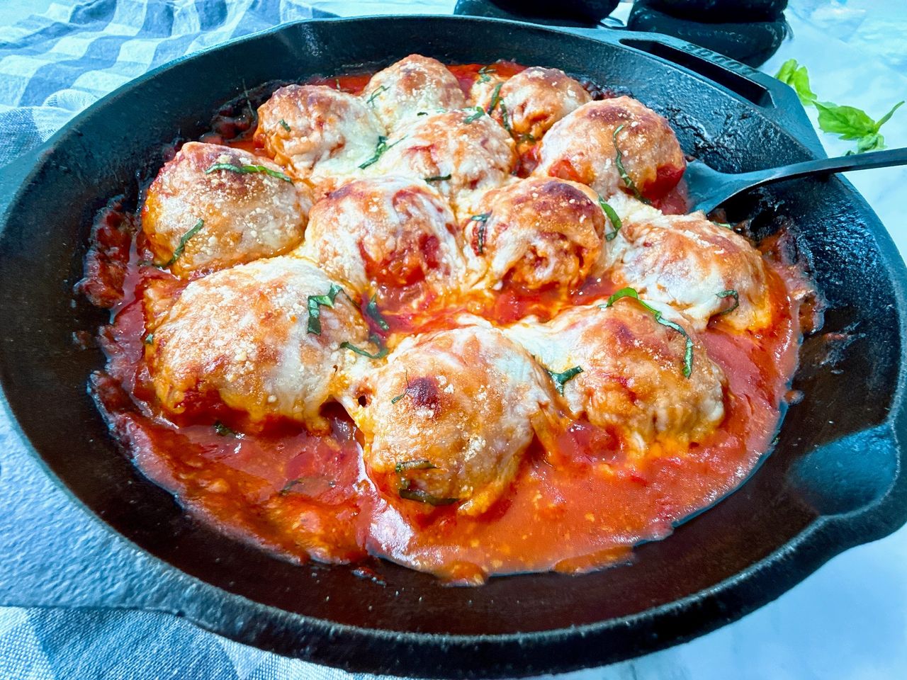 Chicken Parmesan Meatballs in a cast iron skillet with a black spoon and fresh basil