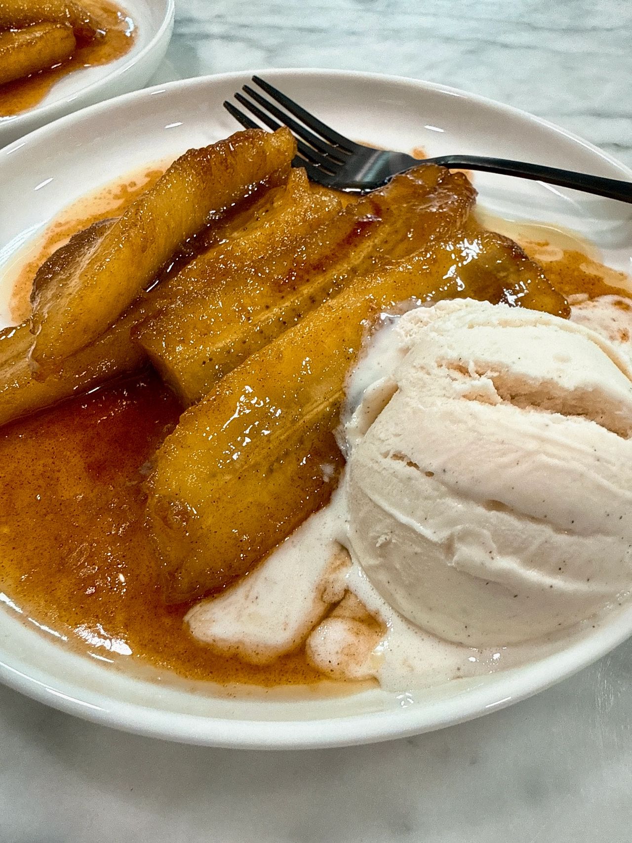 Bananas foster on a white plate with black spoon and vanilla ice cream