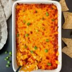 Buffalo Chicken Dip in a white dish with corn chips on a black surface