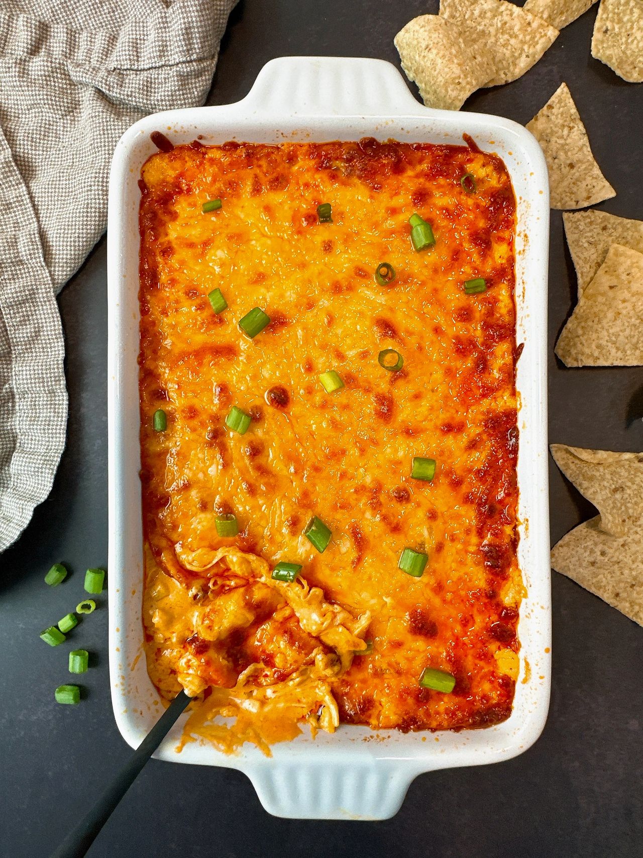Buffalo Chicken Dip in a white dish with corn chips on a black surface