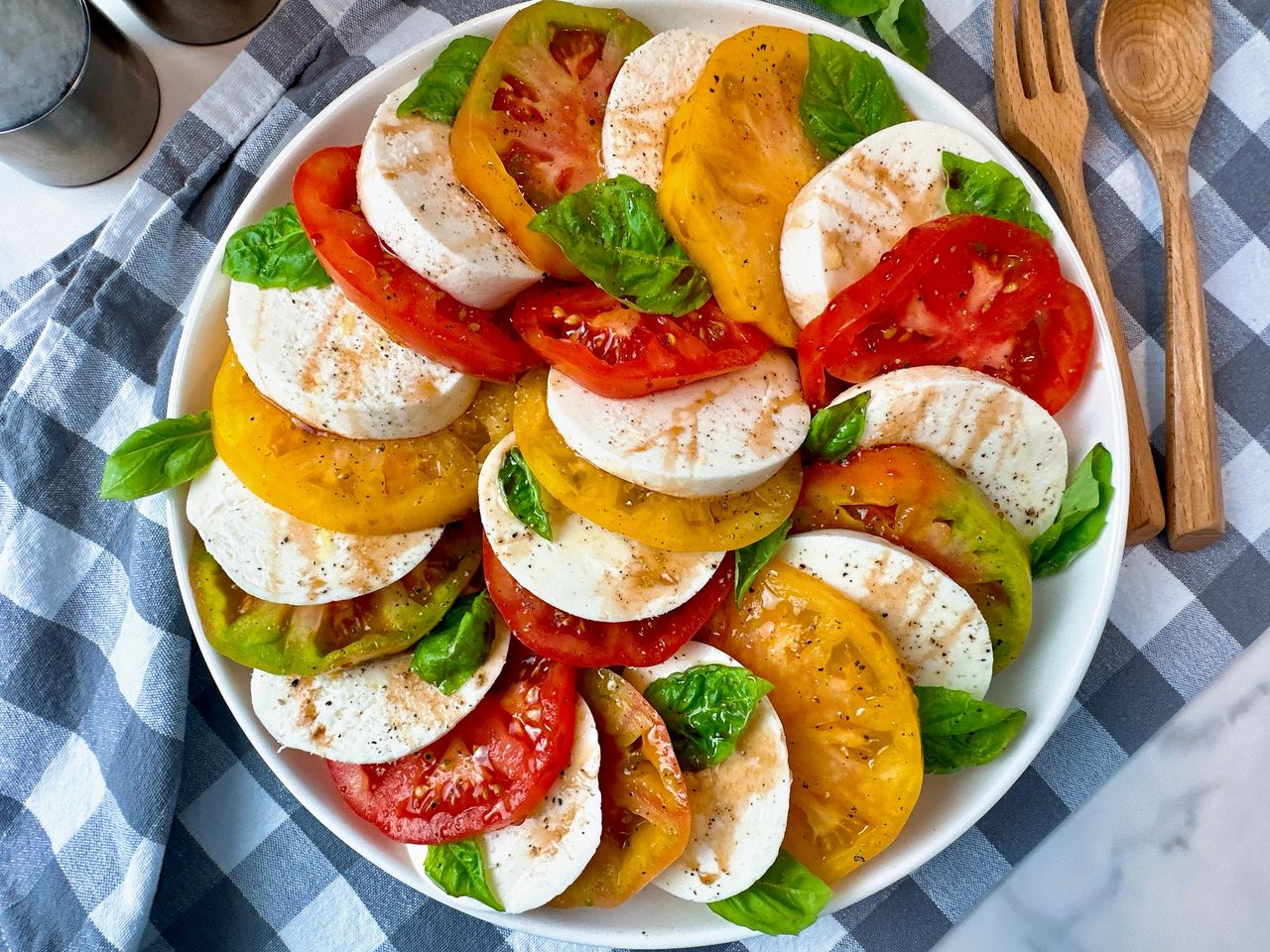 Caprese Salad in a white bowl on a checkered towel with fresh basil leaves