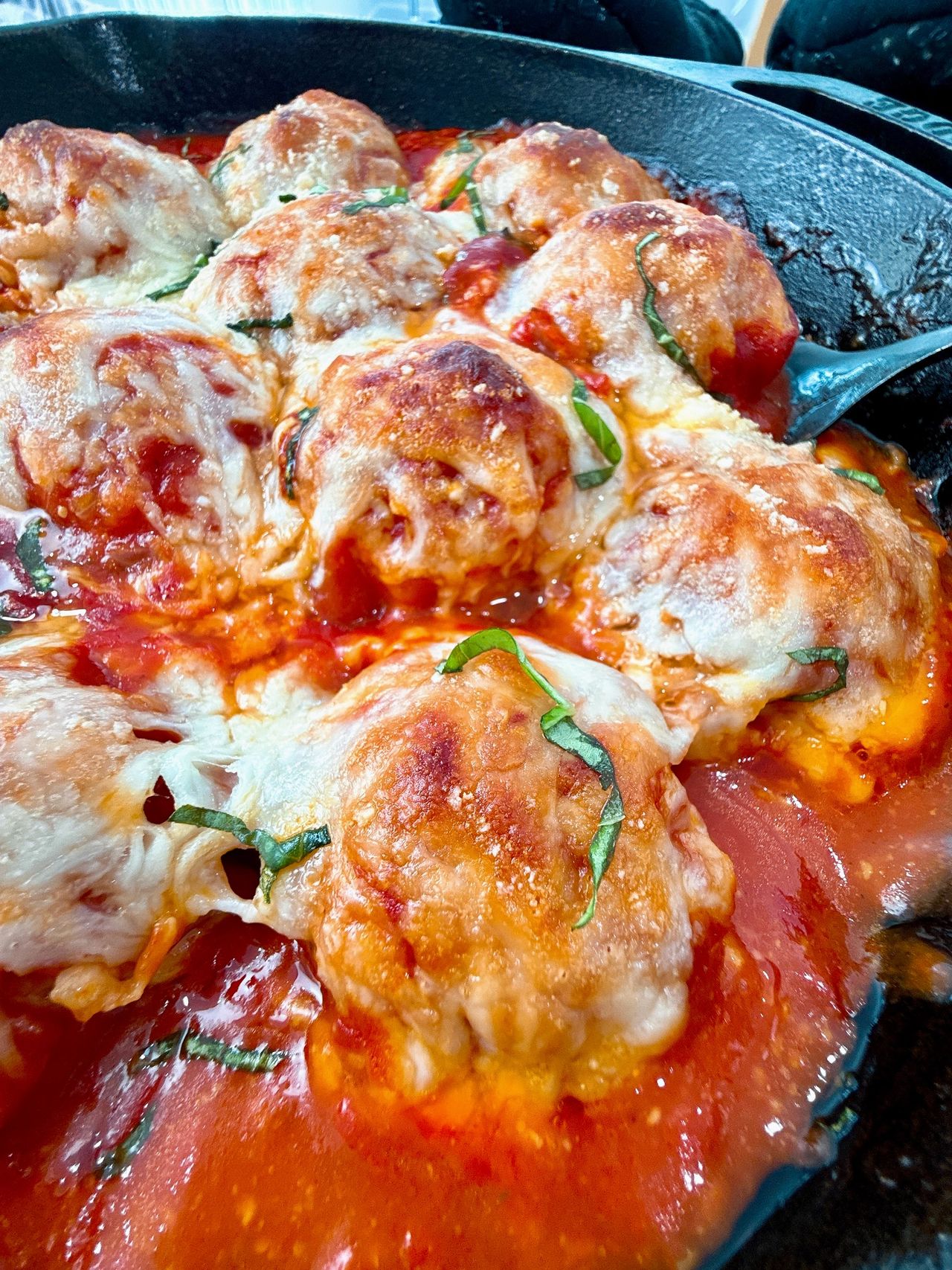 Chicken Parmesan Meatballs in a cast iron skillet with a black spoon and fresh basil