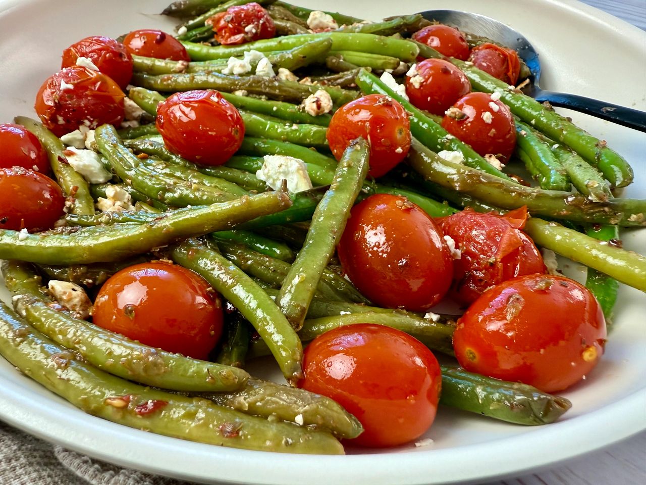 Sautéed Green Beans and Tomatoes in a white skillet with a black spoon