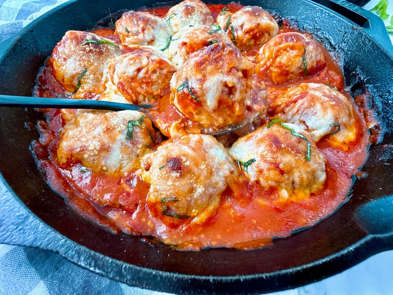 Chicken Parmesan Meatballs in a cast iron skillet with a black spoon and fresh basil