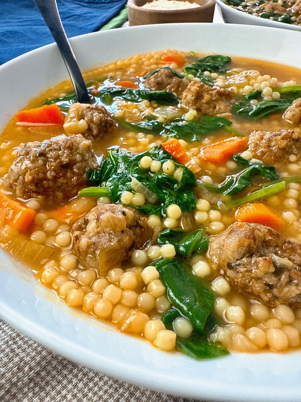 Italian wedding soup in a white bowl with a black spoon