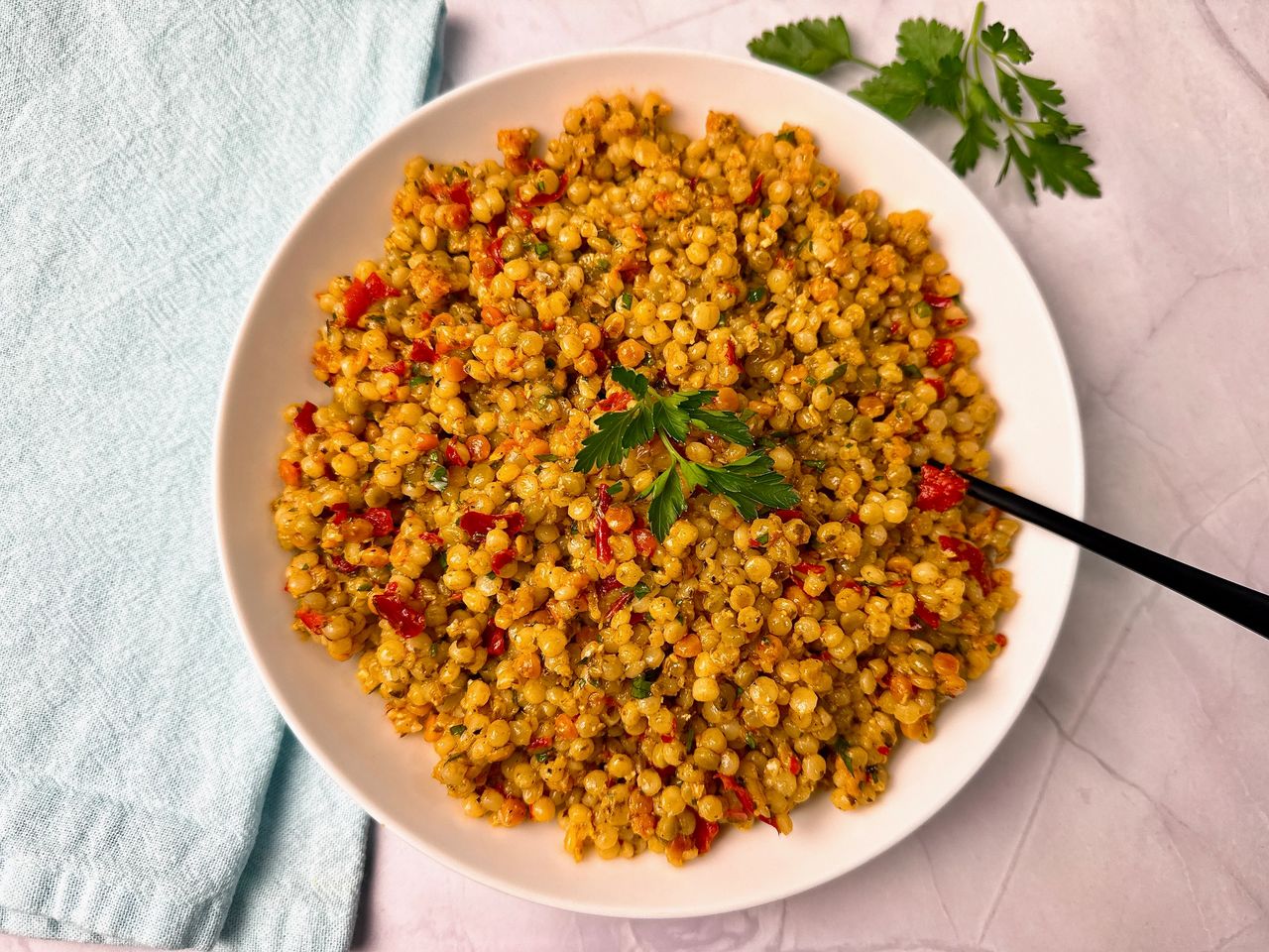 Couscous with Pesto and Peppers in a white bowl with a black spoon and fresh parsley