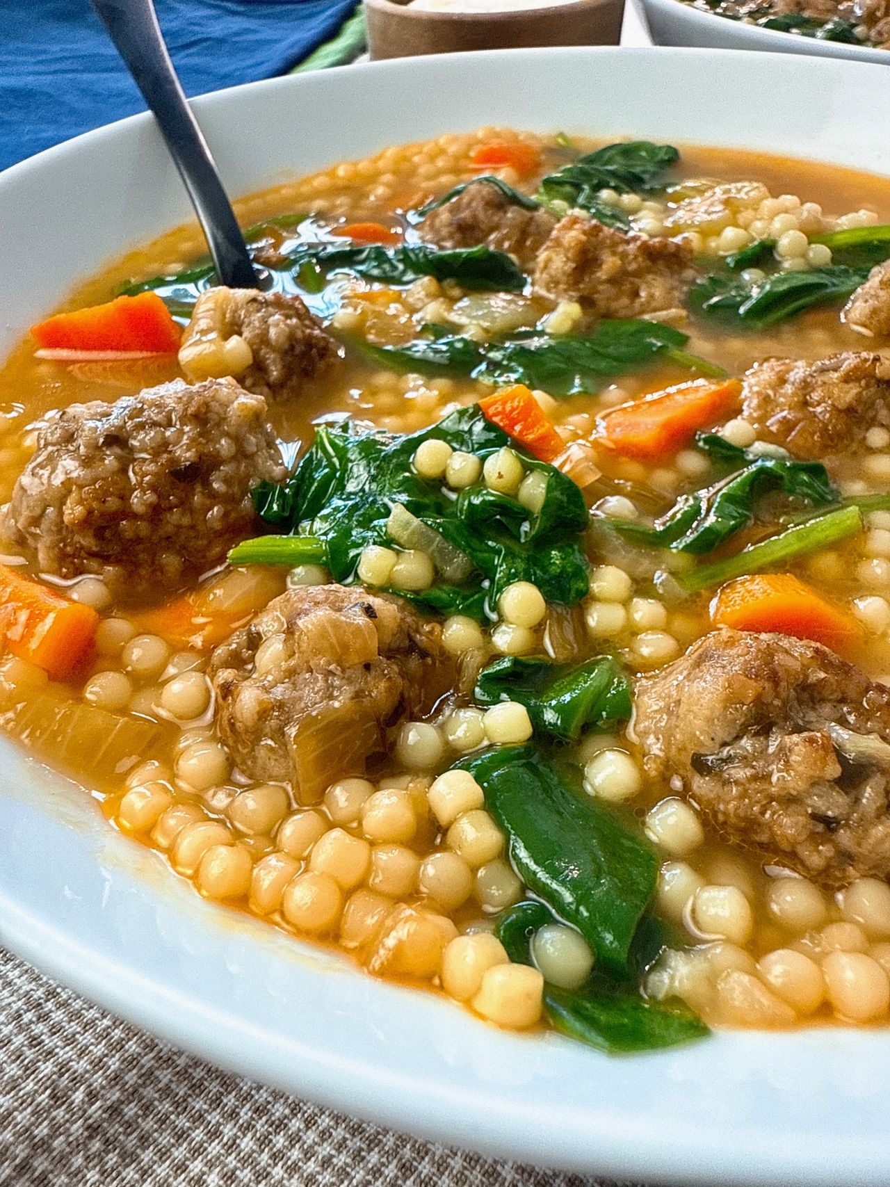 Italian wedding soup in a white bowl with a black spoon