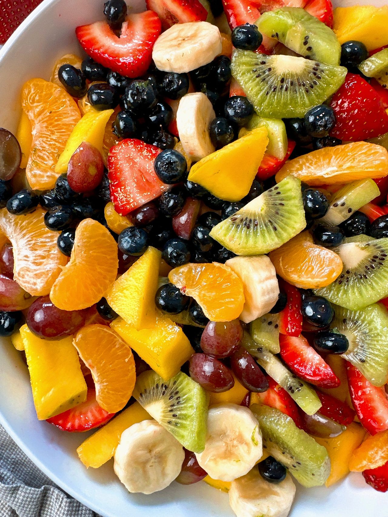 Fruit Salad in a white bowl with a black spoon and honey on the side