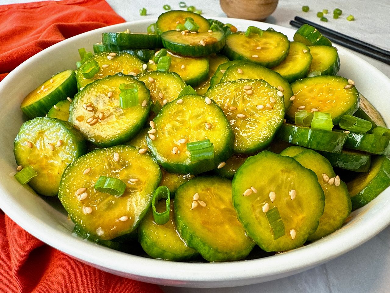 Asian Cucumber Salad in a white bowl with black chop sticks and red napkin