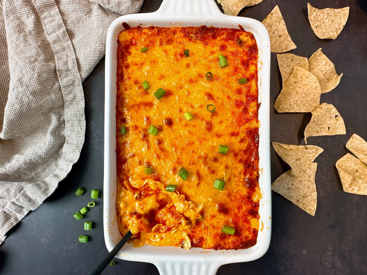 Buffalo Chicken Dip in a white dish with corn chips on a black surface