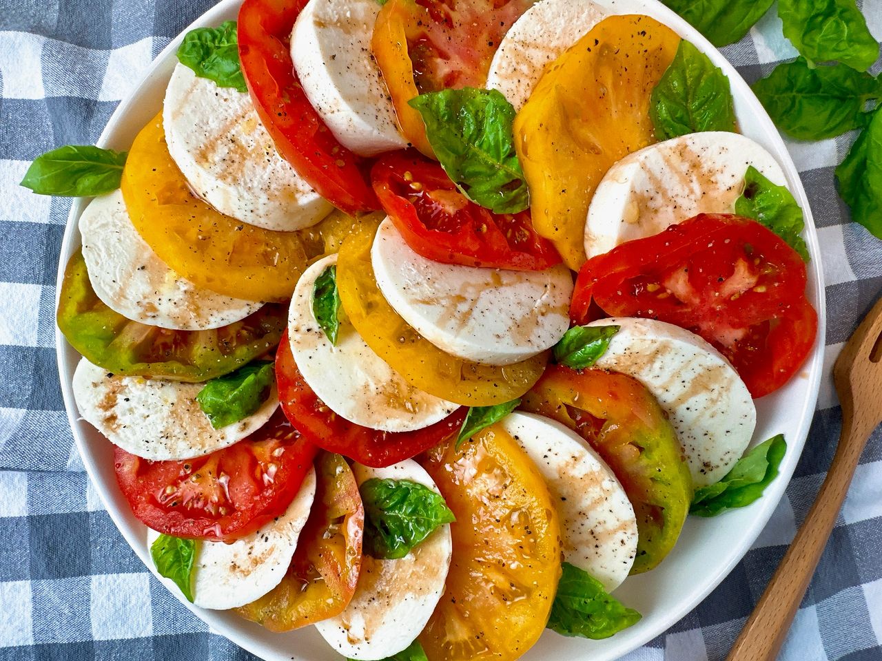 Caprese Salad in a white bowl on a checkered towel with fresh basil leaves