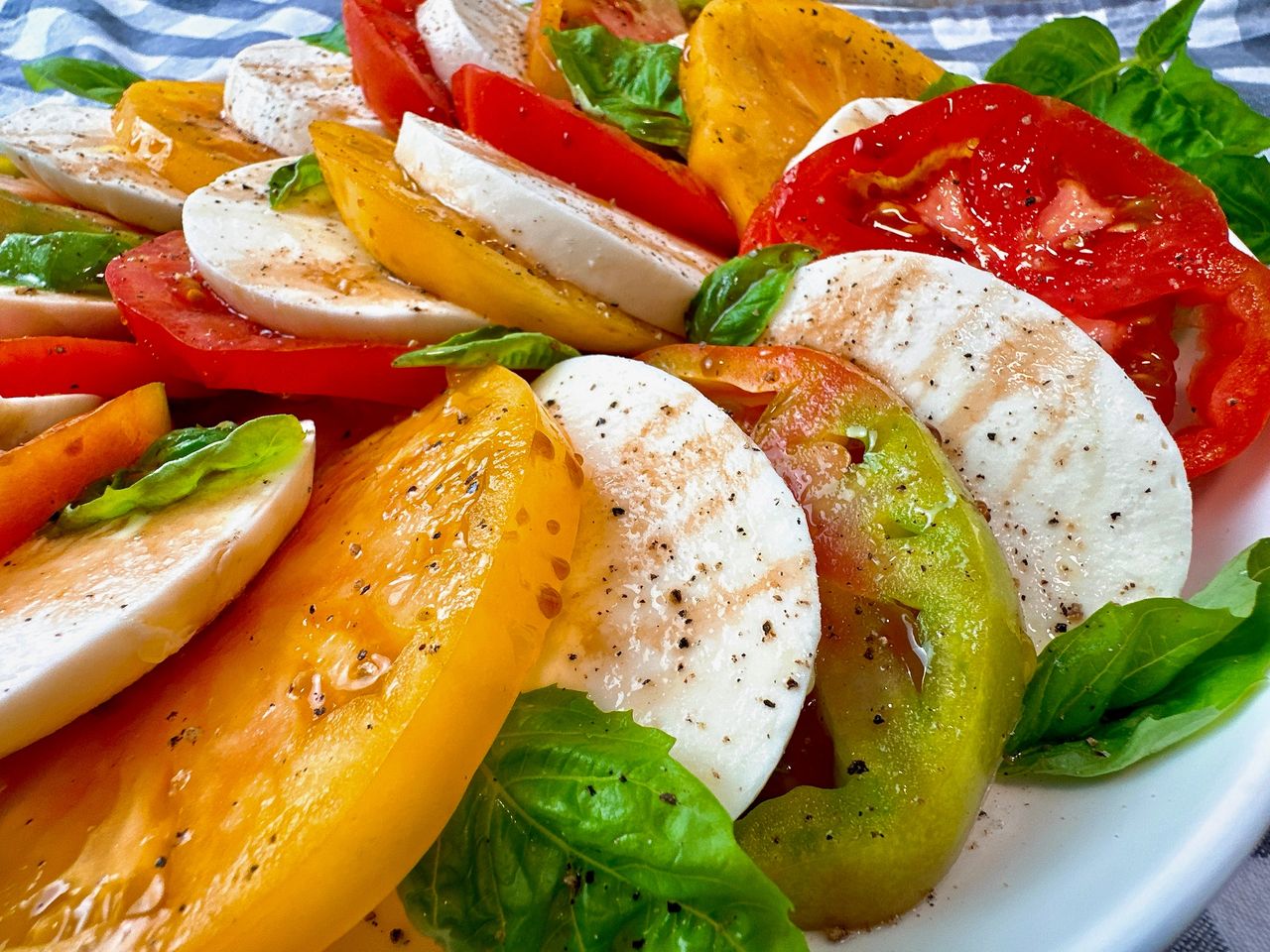 Caprese Salad in a white bowl on a checkered towel with fresh basil leaves