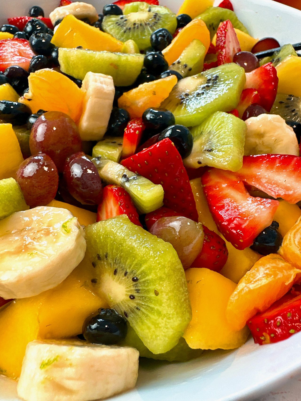 Fruit Salad in a white bowl with a black spoon and honey on the side