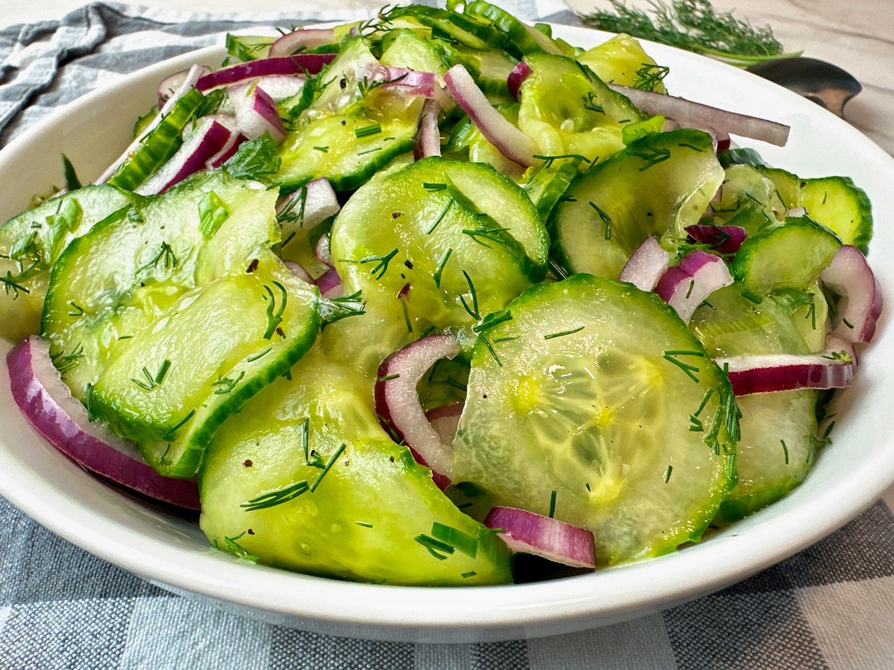 cucumber salad in a white bowl with a black spoon