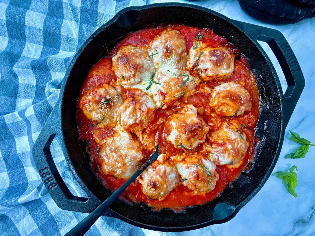 Chicken Parmesan Meatballs in a cast iron skillet with a black spoon and fresh basil