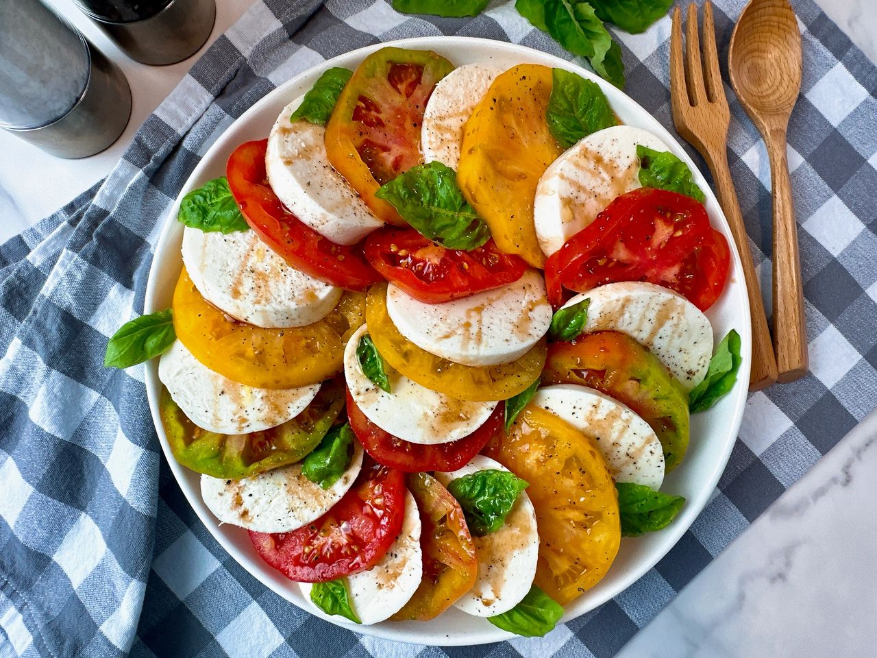 Caprese Salad in a white bowl on a checkered towel with fresh basil leaves