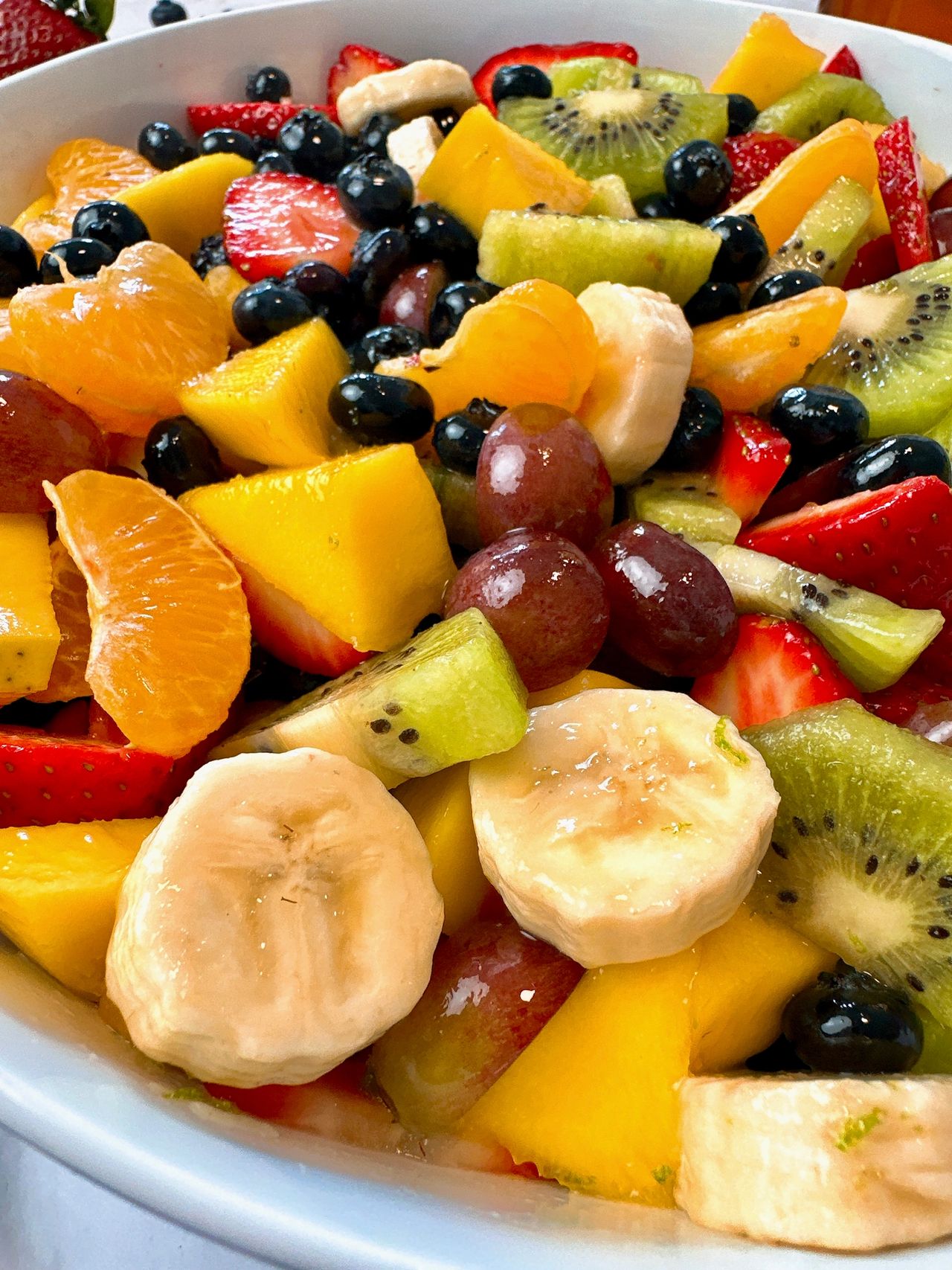 Fruit Salad in a white bowl with a black spoon and honey on the side