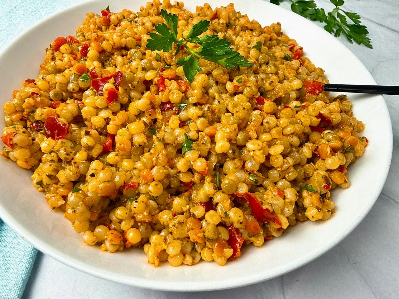 Couscous with Pesto and Peppers in a white bowl with a black spoon and fresh parsley