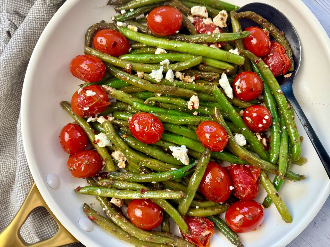 Sautéed Green Beans and Tomatoes in a white skillet with a black spoon