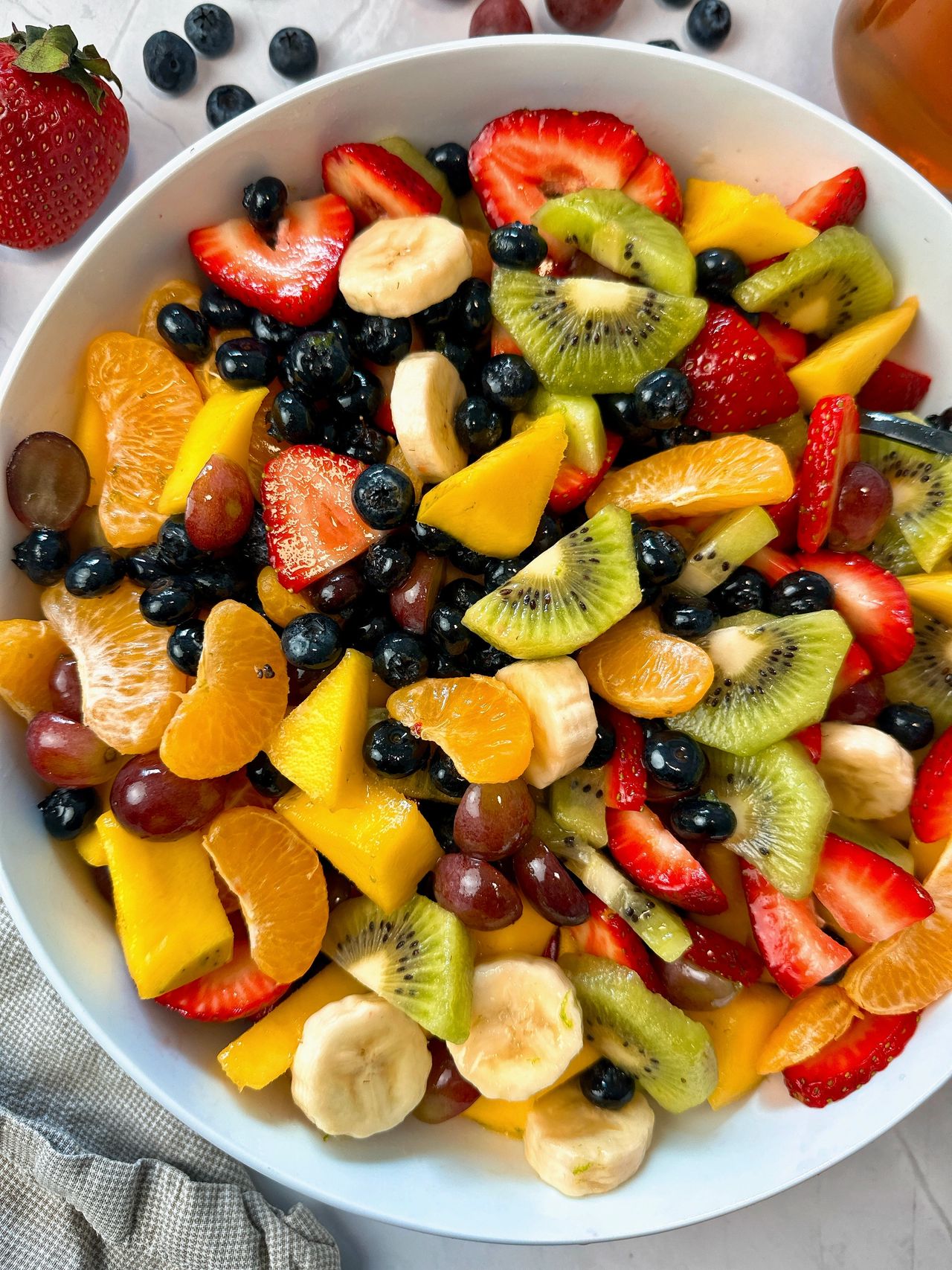 Fruit Salad in a white bowl with a black spoon and honey on the side