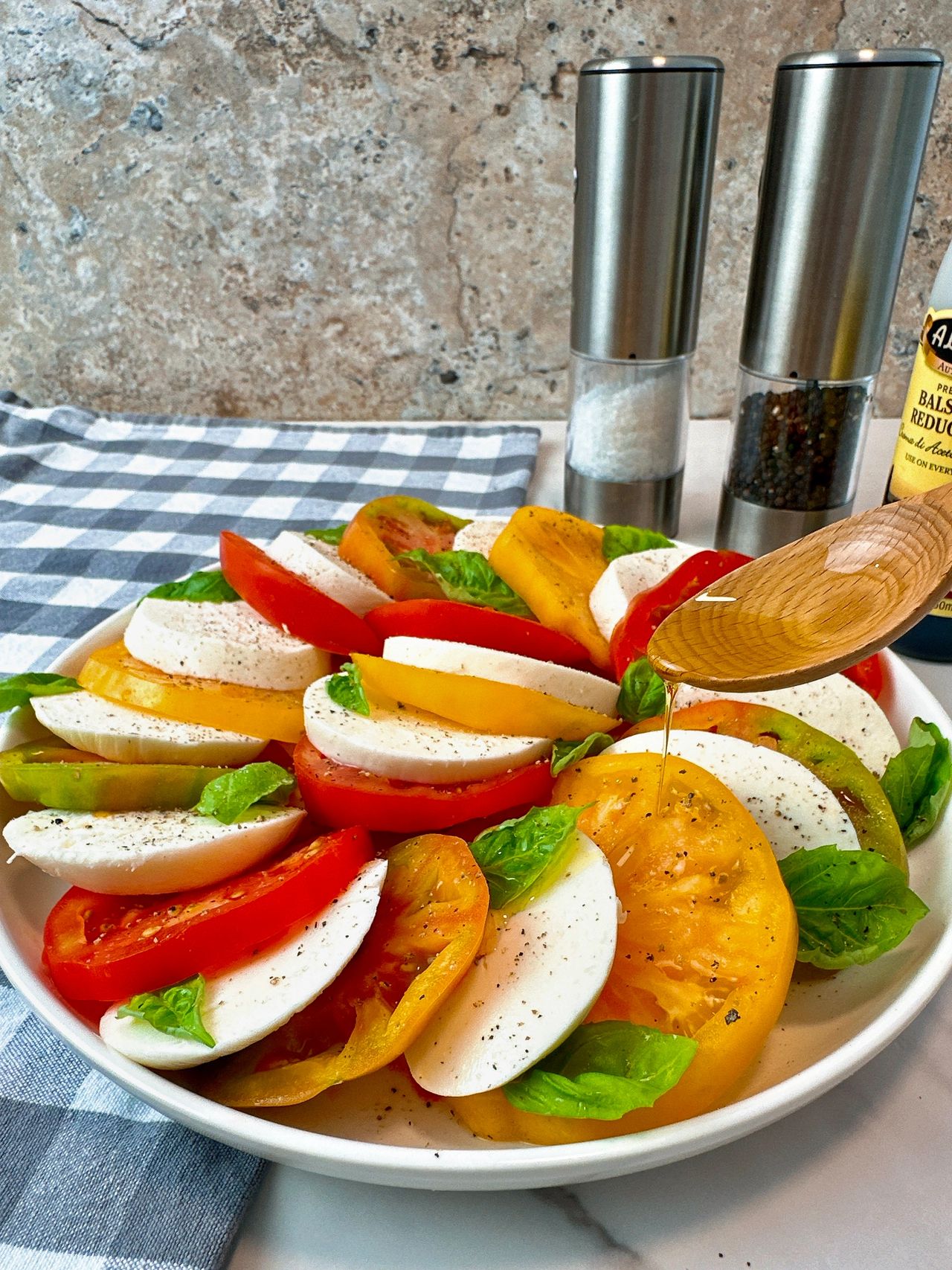 Caprese Salad in a white bowl on a checkered towel with fresh basil leaves