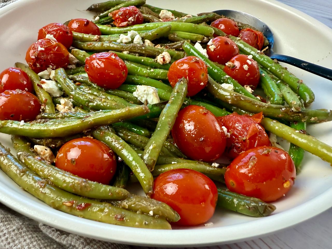 Sautéed Green Beans and Tomatoes in a white skillet with a black spoon