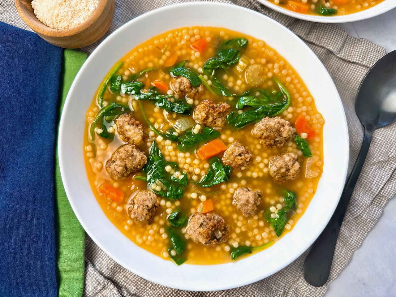 Italian wedding soup in a white bowl with a black spoon