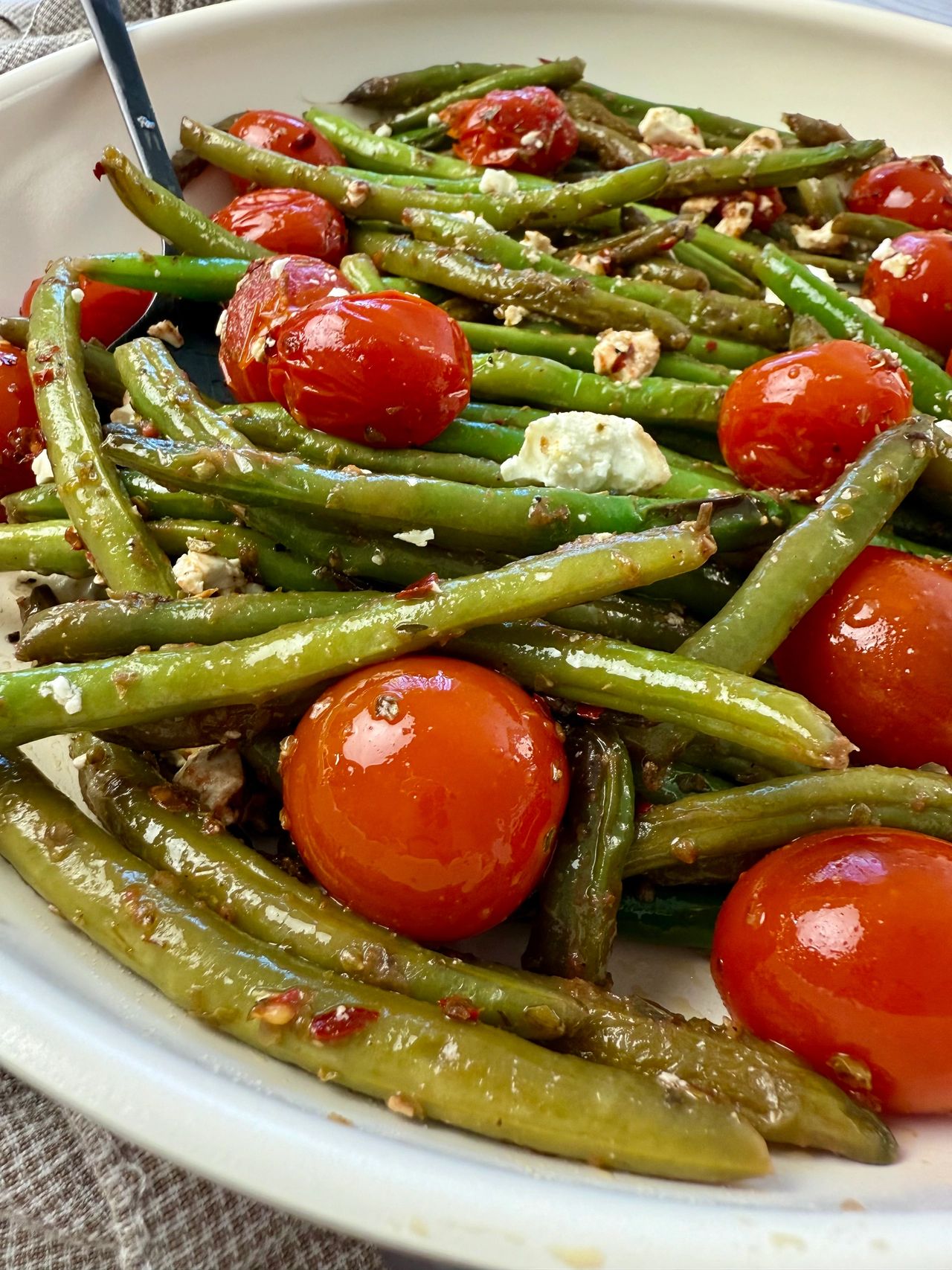 Sautéed Green Beans and Tomatoes in a white skillet with a black spoon