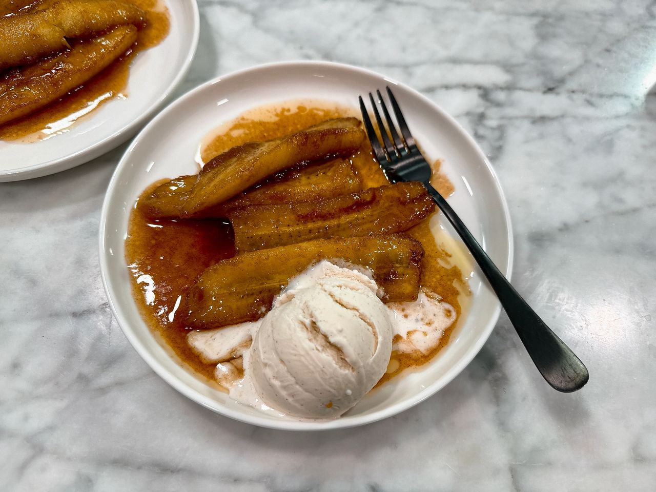 Bananas foster on a white plate with black spoon and vanilla ice cream