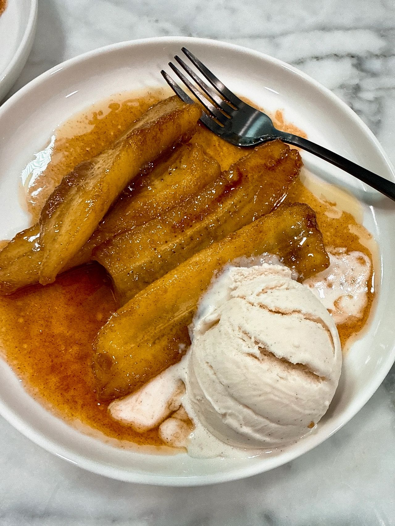 Bananas foster on a white plate with black spoon and vanilla ice cream