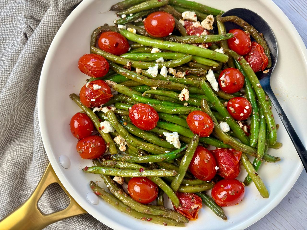 Sautéed Green Beans and Tomatoes in a white skillet with a black spoon