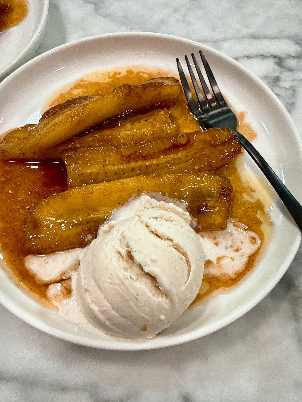 Bananas foster on a white plate with black spoon and vanilla ice cream
