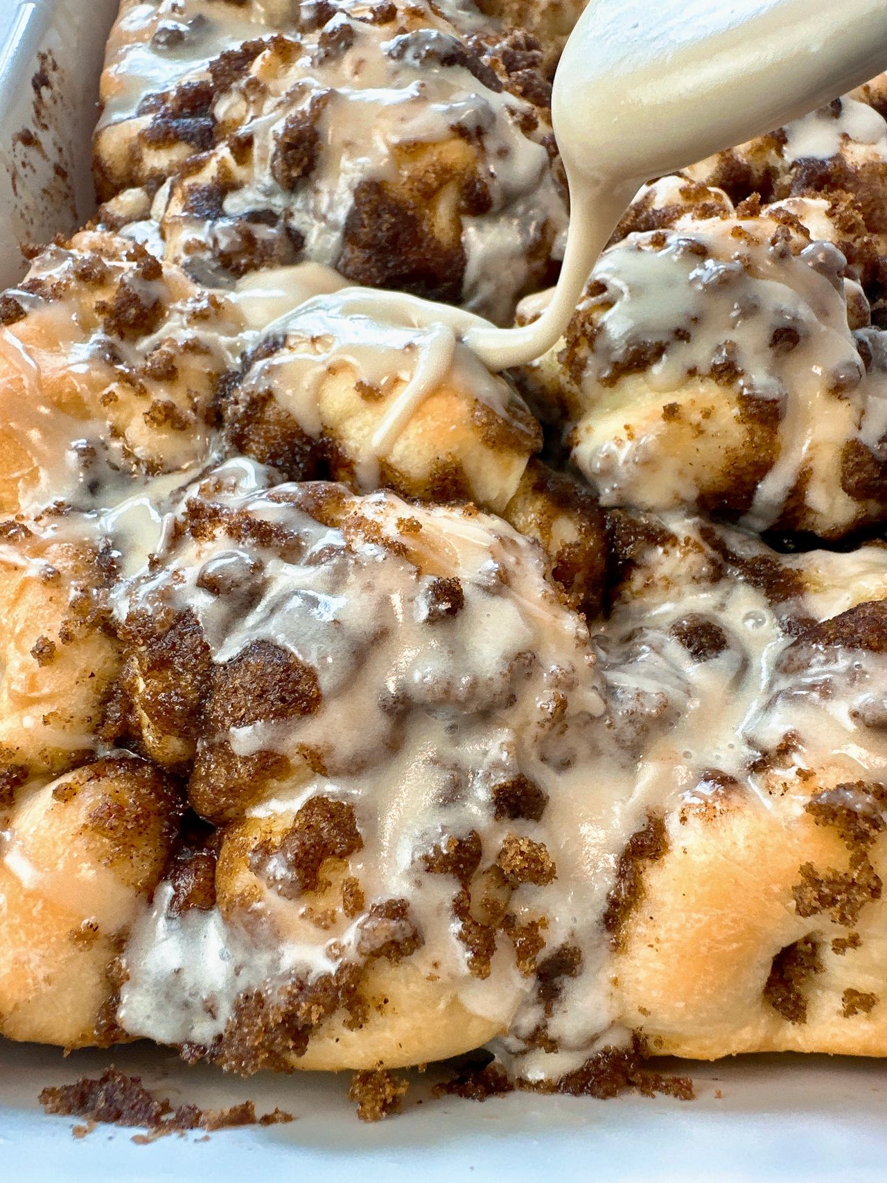 cinnamon roll focaccia in a white baking dish with a spoon of vanilla glaze over top